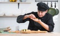 Young attractive Asian chef with black uniform and hat, preparing delicious fresh sushi, putting salmon on rice in a restaurant