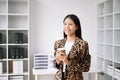 Young attractive Asian female office worker business suits smiling at camera with working notepad, tablet and laptop documents .