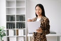 Young attractive Asian female office worker business suits smiling at camera with working notepad, tablet and laptop documents .