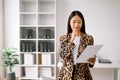 Young attractive Asian female office worker business suits smiling at camera with working notepad, tablet and laptop documents .