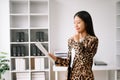 Young attractive Asian female office worker business suits smiling at camera with working notepad, tablet and laptop documents .