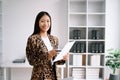 Young attractive Asian female office worker business suits smiling at camera with working notepad, tablet and laptop documents .