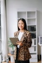 Young attractive Asian female office worker business suits smiling at camera with working notepad, tablet and laptop documents .