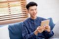 Young attractive asian man resting using browsing tablet computer on sofa at home. Royalty Free Stock Photo