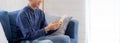 Young attractive asian man resting using browsing tablet computer on sofa at home, happy male sitting on couch. Royalty Free Stock Photo