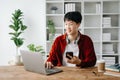 Young attractive Asian man smiling thinking planning writing in notebook, tablet and laptop working from home at home office Royalty Free Stock Photo