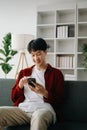 Young attractive Asian man smiling thinking planning writing in notebook, tablet and laptop working from home at home office Royalty Free Stock Photo
