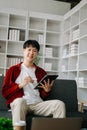 Young attractive Asian man smiling thinking planning writing in notebook, tablet and laptop working from home at home office Royalty Free Stock Photo