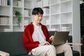 Young attractive Asian man smiling thinking planning writing in notebook, tablet and laptop working from home at home office Royalty Free Stock Photo