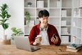 Young attractive Asian man smiling thinking planning writing in notebook, tablet and laptop working from home at home office Royalty Free Stock Photo