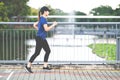 Young attractive asian runner woman running at sidewalk way in public nature city park with lake water
