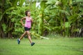 Young attractive Asian sport runner woman running in the jungle smiling happy in training workout on herb with palm trees on the b Royalty Free Stock Photo