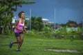 Young attractive Asian sport runner woman running in the jungle smiling happy in training workout on herb with palm trees on the b Royalty Free Stock Photo