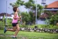 Young attractive Asian sport runner woman running in the jungle smiling happy in training workout on herb with palm young attracti Royalty Free Stock Photo
