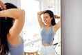 A young attractive Asian woman in casual clothes combs in front of the mirror at home. A charming female Korean smiles and does