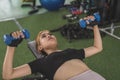 A young and attractive asian woman does bench presses with a pair of blue rubberized dumbbells. Working out chest and upper body