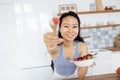 A young attractive Asian woman eats fresh berries in the kitchen. A charming girl holds a plate with raspberries, strawberries and