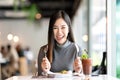 Young attractive asian woman holding fork and spoon feeling hungry, excited, happy and ready to eat healthy food looking at camera