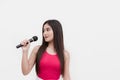 A young attractive asian woman in a pink sleeveless top using a microphone to sing or host an event. Isolated on a white Royalty Free Stock Photo