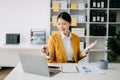 Young attractive Asian woman smiling thinking planning writing in notebook, tablet and laptop working from home, looking at camera Royalty Free Stock Photo