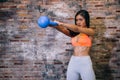 Young attractive athlete muscular woman in sportswear exercising crossfit workout with kettle bell over red brick background.