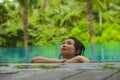 Young attractive and beautiful Asian Korean woman relaxing happy at tropical beach resort swimming at jungle infinity pool Royalty Free Stock Photo