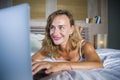 Young attractive and beautiful happy Caucasian woman 30s lying in bed at home using internet working on computer laptop smiling re Royalty Free Stock Photo