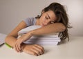 Young attractive and beautiful tired student girl leaning on school books pile sleeping tired and exhausted after studying