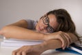 Young attractive and beautiful tired student girl leaning on school books pile sleeping tired and exhausted after studying Royalty Free Stock Photo