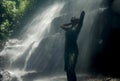 Young attractive and blissful Asian Indonesian woman overwhelmed by the beauty and purity of natural waterfall in tropical jungle Royalty Free Stock Photo