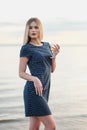 A young attractive blond woman, in a blue dress, walks along the seashore. Portrait of a smiling woman on vacation with Royalty Free Stock Photo