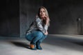 Young attractive blond woman in fashionable green cowboy boots in a vintage shirt in stylish ripped jeans sits in a dark gray room Royalty Free Stock Photo