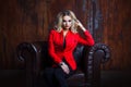 Young and attractive blond woman in red jacket sits in leather armchair, background grunge rusty wall Royalty Free Stock Photo