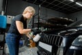 Young attractive blond woman, worker of car detailing service, removing dust from car radiator grille using aero gun for Royalty Free Stock Photo