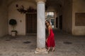 Young, attractive, blonde woman in an elegant red party dress leaning on a marble column smiling happily. Concept beauty, fashion Royalty Free Stock Photo