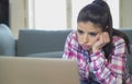 Young attractive and bored latin woman on her 30s working at home living room sitting on couch with laptop computer in stress look