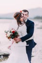 Young attractive bridal couple holding each other on pebble riverside with forest hills as background Royalty Free Stock Photo