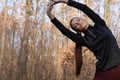 Young attractive brunet slim woman in sportswear doing stretching exercise for hand in autumn forest. Warm up before Royalty Free Stock Photo