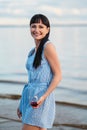 A young attractive brunette woman, in a blue dress, walks along the seashore. Portrait of a smiling woman on vacation Royalty Free Stock Photo