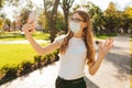 Young attractive business woman in a medical protective mask on her face, talking on a video call on a smartphone, on the street Royalty Free Stock Photo