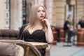 Young attractive business woman sitting at table in street cafe in black suit and waiting her order. Lonely woman Royalty Free Stock Photo