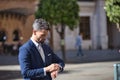 Young and attractive businessman, with beard and suit, standing in the middle of a city street looking at the time on his watch. Royalty Free Stock Photo