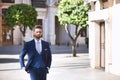 Young and attractive businessman, with beard and suit, walking along a city street with his hand in his pocket. Concept beauty, Royalty Free Stock Photo