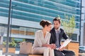 Young attractive businessman discussing business plans over document with beautiful businesswoman while sitting on bench against Royalty Free Stock Photo