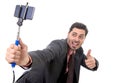 Young attractive businessman in suit and tie taking selfie photo with mobile phone camera and stick posing happy Royalty Free Stock Photo