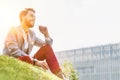 Young attractive businessman talking on smartphone with earphones on while sitting on the grass Royalty Free Stock Photo