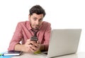 Young attractive businessman working at office desk with mobile phone and computer laptop looking bored and tired Royalty Free Stock Photo