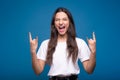 Young and attractive caucasian or arab brunette girl in white t-shirt showing rocker and punk gesture with fingers and screaming i