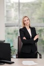 Young attractive Caucasian blond woman in black business suit sits at desk in bright office. Studying paper documents Royalty Free Stock Photo