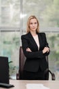 Young attractive Caucasian blond woman in black business suit sits at desk in bright office. Studying paper documents Royalty Free Stock Photo